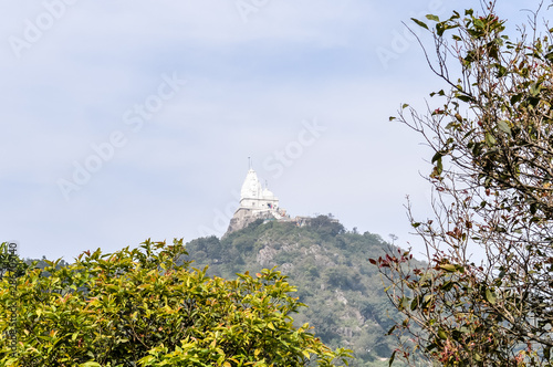 Shikharji Temple, the holiest Jain Teerths, on top of Parasnath Hill peak in Parasnath Range. The white pagoda style temple is located on the mountaintop surrounded by trees in jungle with mist on top