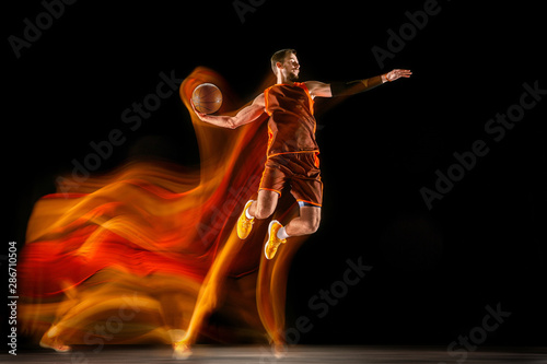 The fire tracks. Young caucasian basketball player of red team in action and jump in mixed light over dark studio background. Concept of sport, movement, energy and dynamic, healthy lifestyle. © master1305