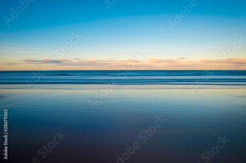 Scenic view of the glassy smooth shore of a deserted beach during the magic hour of sunset
