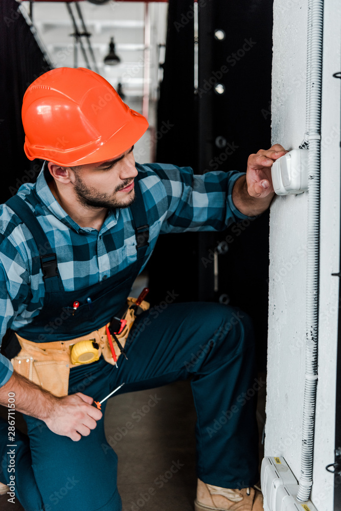 handsome bearded worker in safety helmet touching light switch