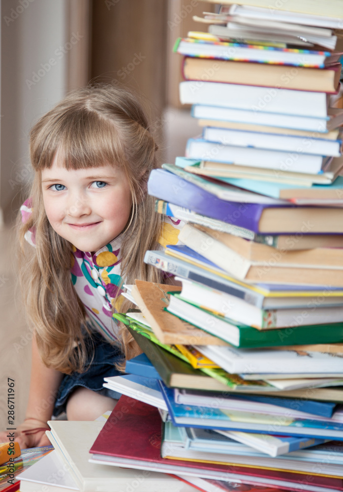 A charming little girl peeks out from behind a stack of books. A charming little girl peeks out from behind a stack of books.