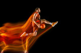 High flight. Young caucasian basketball player of red team in action and motion in mixed light over dark studio background. Concept of sport, movement, energy and dynamic, healthy lifestyle.