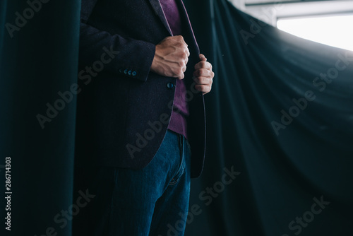 cropped view of stylish young man in jacket standing near curtain