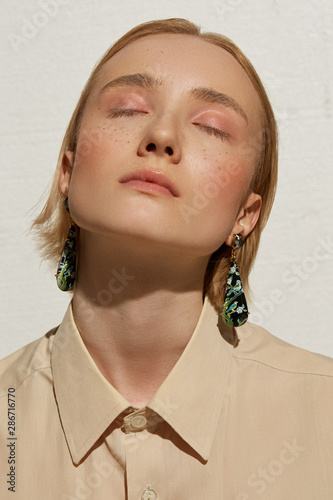 Cropped portrait shot of a young blonde European lady with stud earrings with large gray facetted gems on the earlobes and hanging tearshaped pendants with a drawing.  photo