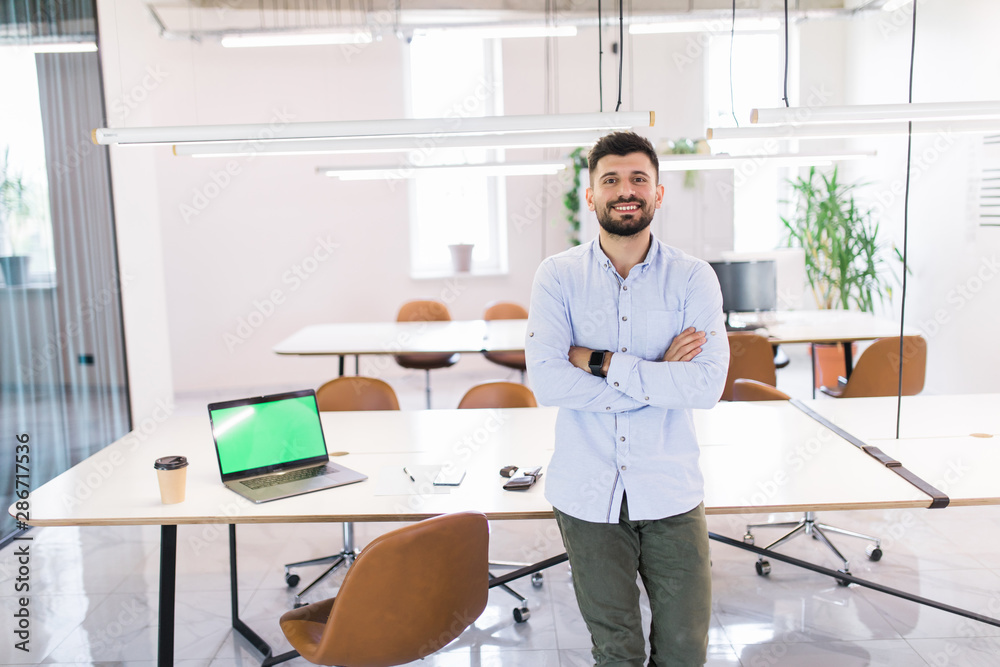Portrait of attractive young man standing with crossed arms in modern office Portrait of attractive young man standing with crossed arms in modern office