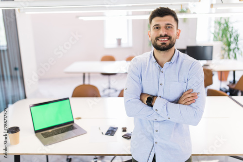 Portrait of attractive young man standing with crossed arms in modern office