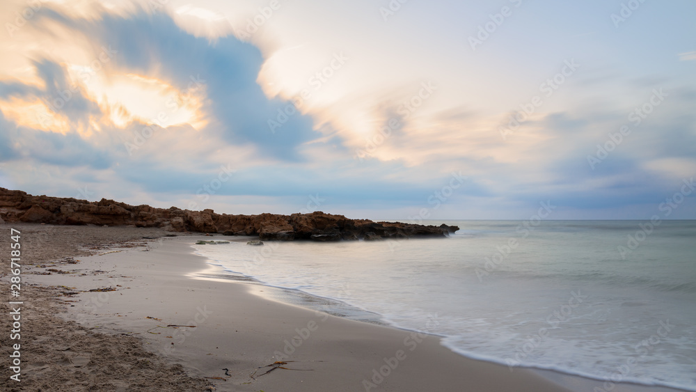 Colorful clouds in the early morning just before sunrise. A bay with sandy beach for swimming near the Spanish town of Torrevieja. Soft waves through long exposure.