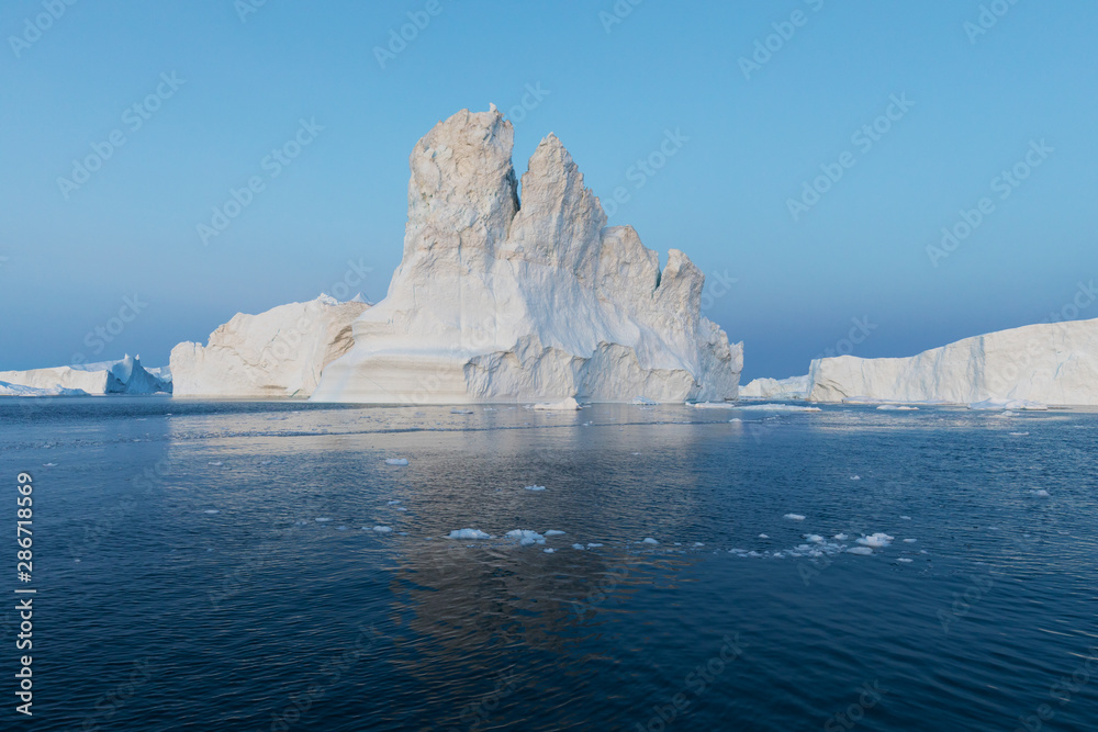 Photogenic and intricate iceberg under an interesting and blue sky during sunset. Effect of global warming in nature. Conceptual image of melting glacier in deep blue water in Antarctica or Greenland