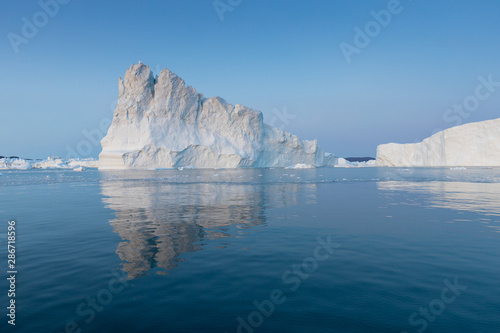 Photogenic and intricate iceberg under an interesting and blue sky during sunset. Effect of global warming in nature. Conceptual image of melting glacier in deep blue water in Antarctica or Greenland © Michal