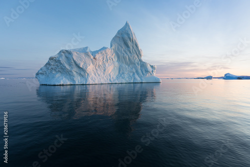 Photogenic and intricate iceberg under an interesting and blue sky during sunset. Effect of global warming in nature. Conceptual image of melting glacier in deep blue water in Antarctica or Greenland photo