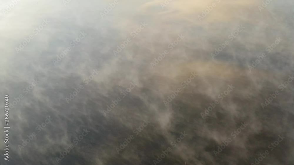 Drone flight during morning sunrise above misty lake with sky reflection Drone flight during morning sunrise above misty lake with sky reflection