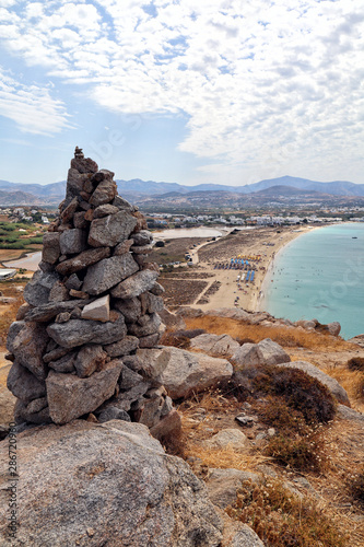 A cairn of stones on a hilltop overlooking beach of Agios Prokopios and turquoise Aegean Sea, Naxos, Greek Islands photo