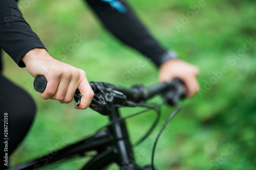 Steering wheel bike close-up. A man is riding a bicycle in a forest in the open air close-up. Park, active recreation, sports and a healthy lifestyle. Hands of a man on the wheel of a bicycle.