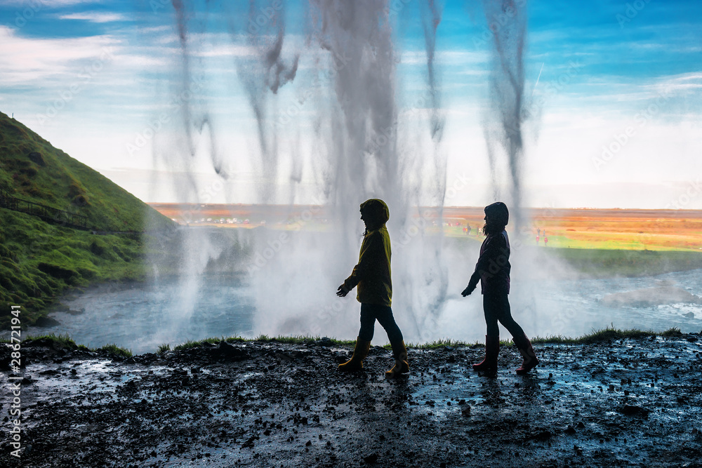two girls walking under a waterfall - obrazy, fototapety, plakaty 