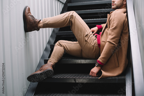 partial view of man in brown coat and wristwatch sitting on stairs