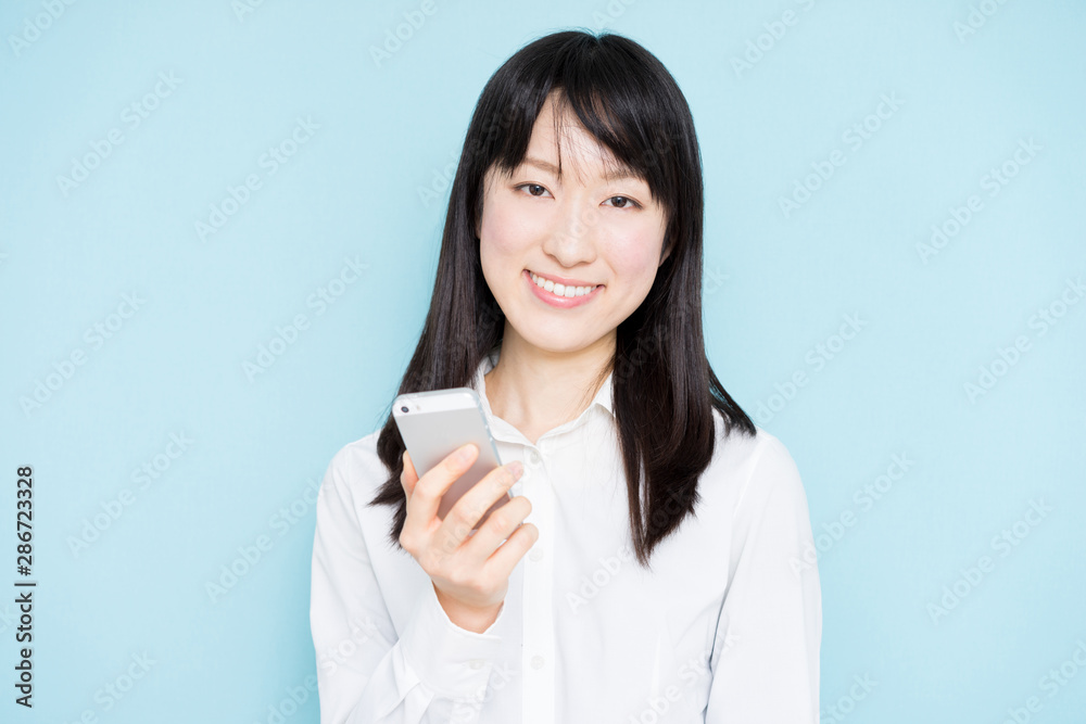 Young business woman holding smart phone against light blue background Young business woman holding smart phone against light blue background