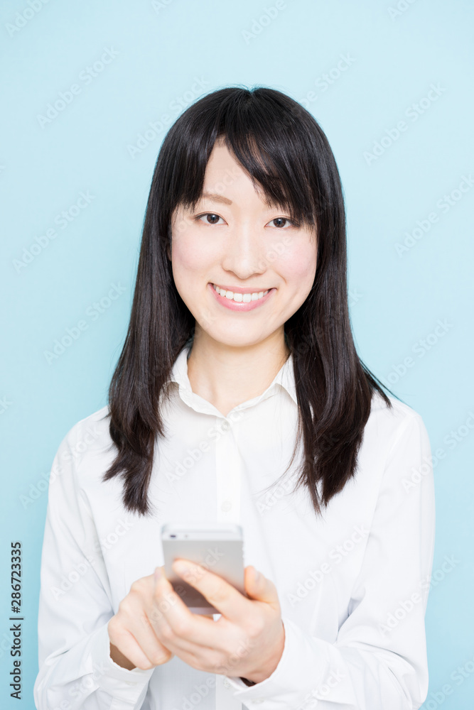 Young business woman holding smart phone against light blue background Young business woman holding smart phone against light blue background