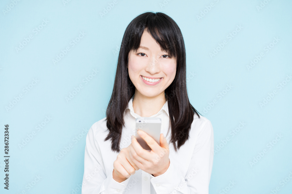 Young business woman holding smart phone against light blue background Young business woman holding smart phone against light blue background