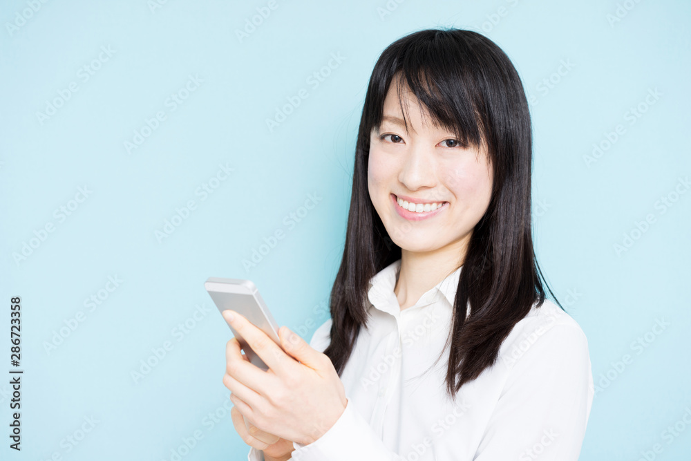 Young business woman holding smart phone against light blue background Young business woman holding smart phone against light blue background