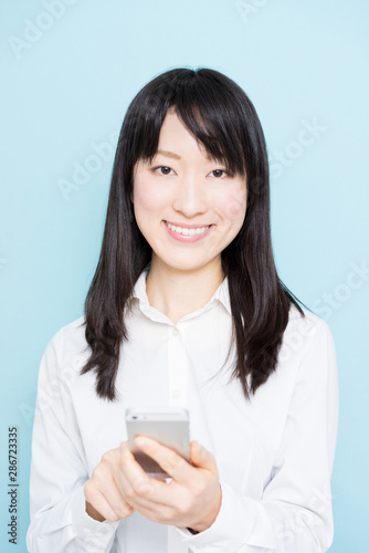 Young business woman holding smart phone against light blue background