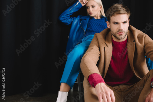 stylish young woman and man in autumn clothes near black curtain