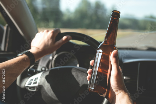 Fotografia, Obraz Driver is driving a car with a bottle of beer in hand