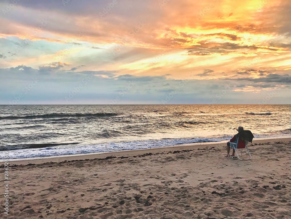 Naklejka premium Older lady alone shoeless is sitting on the chair and looking to the baltic sea during the sunset