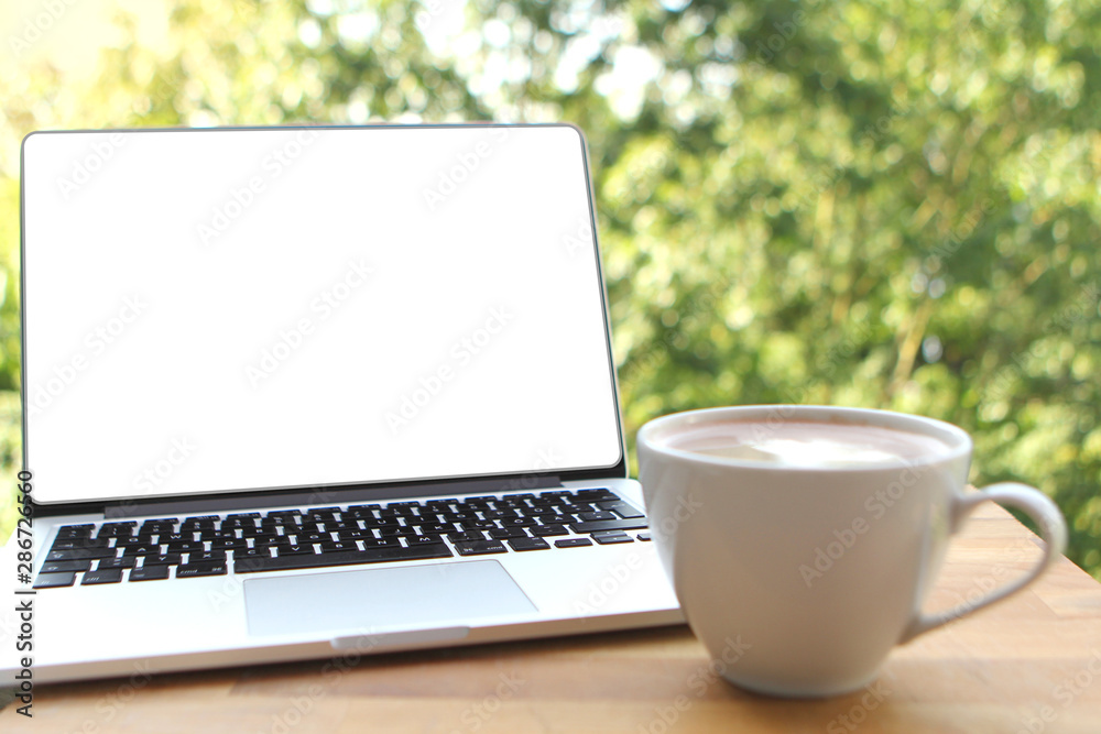 Fototapeta premium Mock up image of a pleasant morning using a laptop with a blank white desktop screen with a cup of coffee on a wooden table in an outdoor cafe