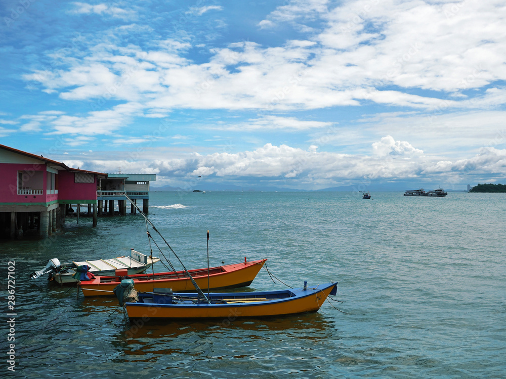 Colorful wooden boats and old houses by the sea. Vibrant blue sky and clouds with far away mountain silhouette.