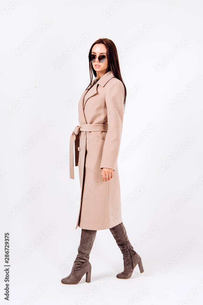 girl in a warm light coat on a white background. model in outerwear. brunette woman in a winter coat and sunglasses. beautiful girl in a casual coat. spring autumn collection girl in a warm light coat on a white background. model in outerwear. brunette woman in a winter coat and sunglasses. beautiful girl in a casual coat. spring autumn collection