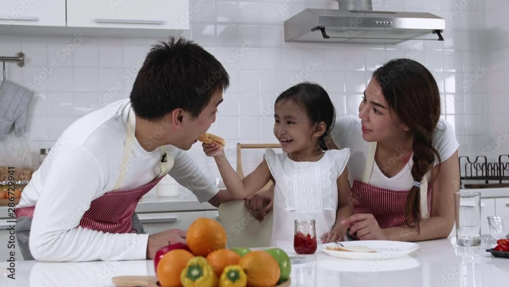 Happy Asian family make a cooking. Father, Mother and Daughter are eating breakfast in the kitchen at home. Bread with jam. Healthy food concept