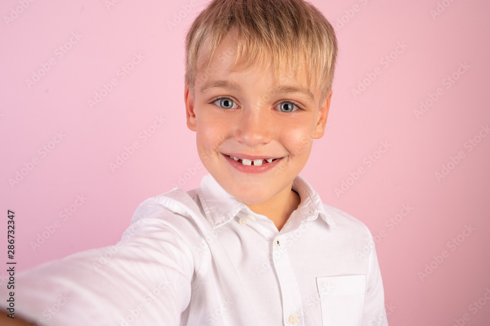 Cheerful selfie. Cheerful young boy in shirt holding mobile phone and making photo of himself while standing against pink background Cheerful selfie. Cheerful young boy in shirt holding mobile phone and making photo of himself while standing against pink background