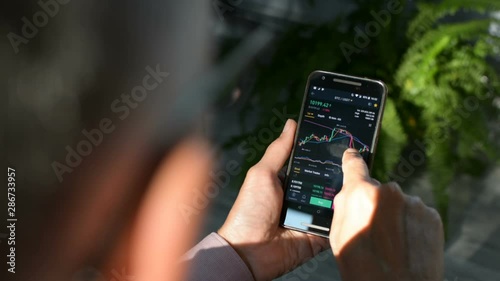 Businessman is checking Bitcoin price chart on crypto exchange on amobile phone screen. Cryptocurrency future price prediction concept.