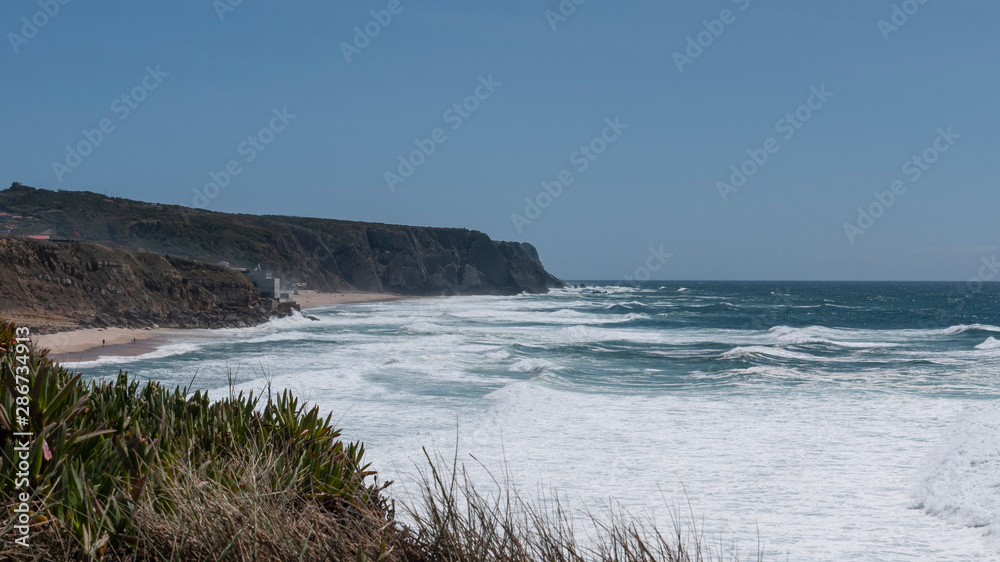 Cliff top view of Praia Grande from Praia das Maçãs, Portugal & the waves of the Atlantic ocean. Taken on a sunny summer day.