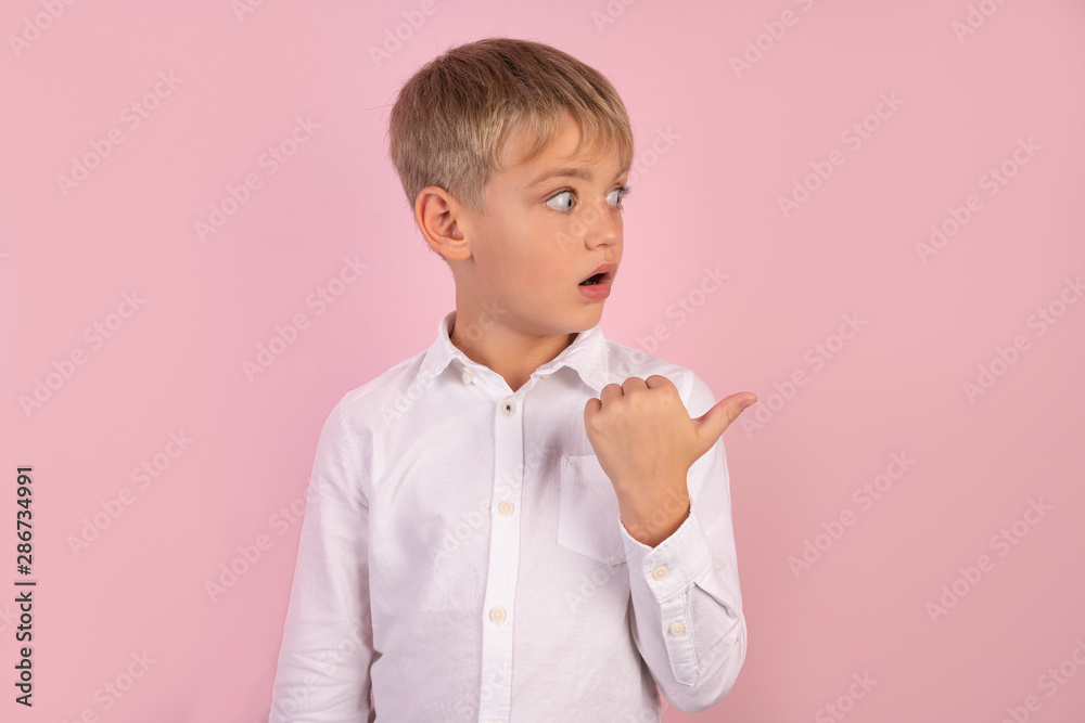 Horizontal shot of attractive amazed European male chiled in fashionable shirt points aside with thumb, shows something against white blank wall, has shocked expression. Lets go in this direction Horizontal shot of attractive amazed European male chiled in fashionable shirt points aside with thumb, shows something against white blank wall, has shocked expression. Lets go in this direction