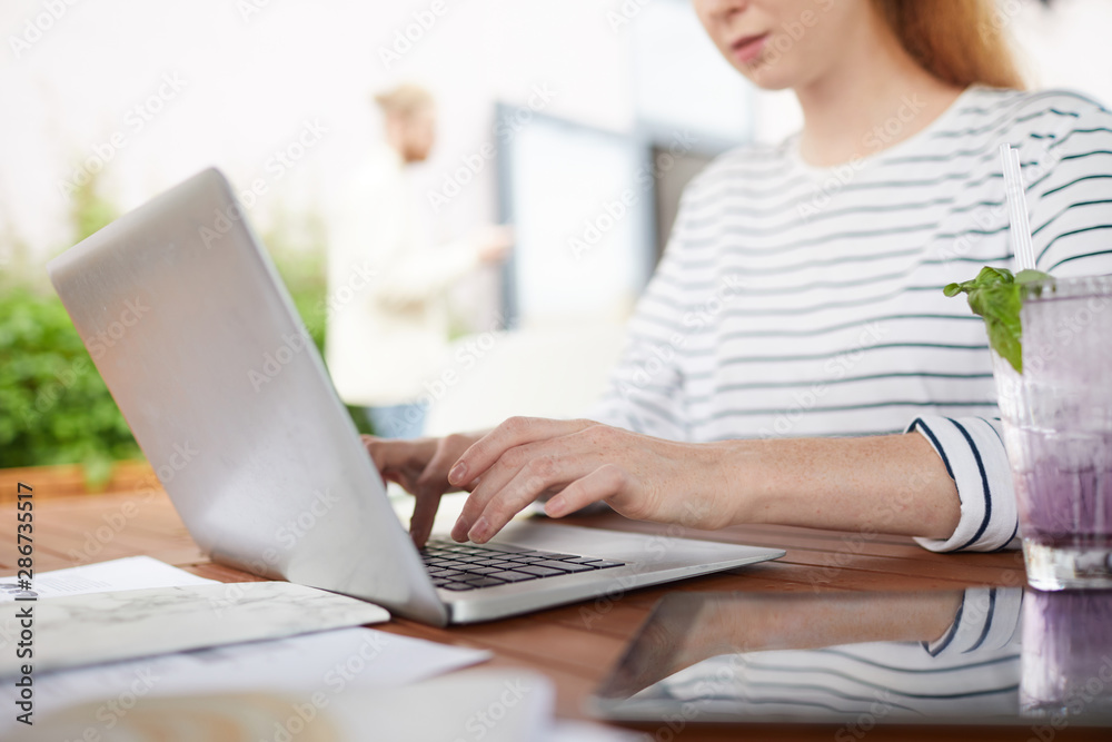 Close-up of young woman sitting at the table and typing on laptop computer she working online in cafe Close-up of young woman sitting at the table and typing on laptop computer she working online in cafe