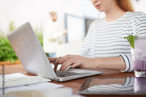 Close-up of young woman sitting at the table and typing on laptop computer she working online in cafe