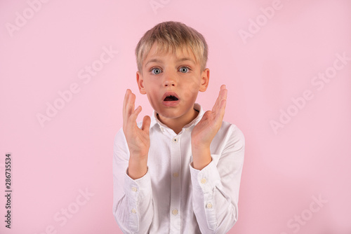 Emotional young male with surprised doubtful expression clasps palms in bewilderment  stares with eyes full of disbelief  reacts on sudden negative news  isolated over pink background