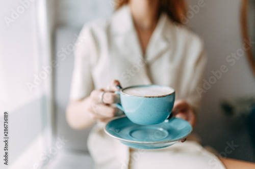  atmospheric coffee shop and stylish dishes. hot mug of coffee in the hands of a young girl.