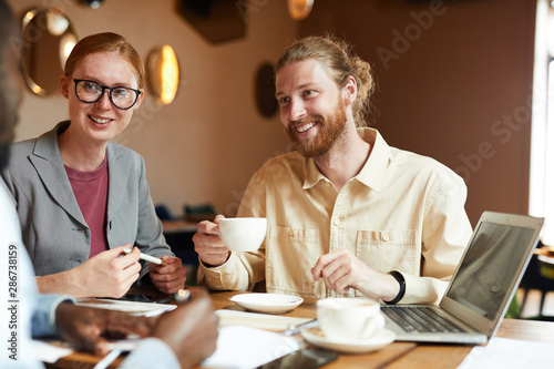 Young business people drinking coffee and talking to the business partner while sitting at the table during meeting in cafe
