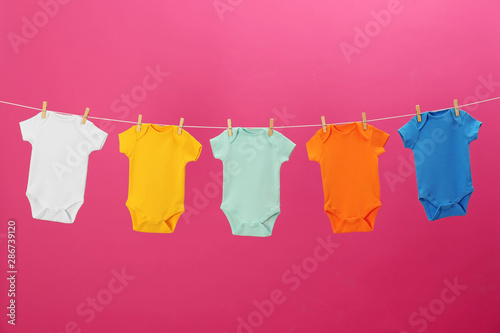 Baby onesies hanging on clothes line against pink background