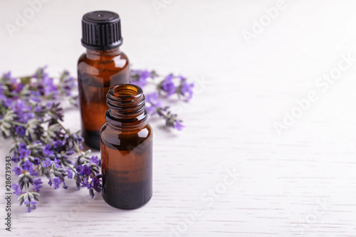 Bottles of essential oil and lavender flowers on white wooden background. Space for text
