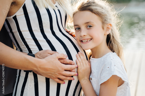 Photo of girl embracing pregnant belly mom in park