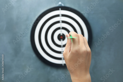 Woman throwing green arrow at dart board on grey background, closeup