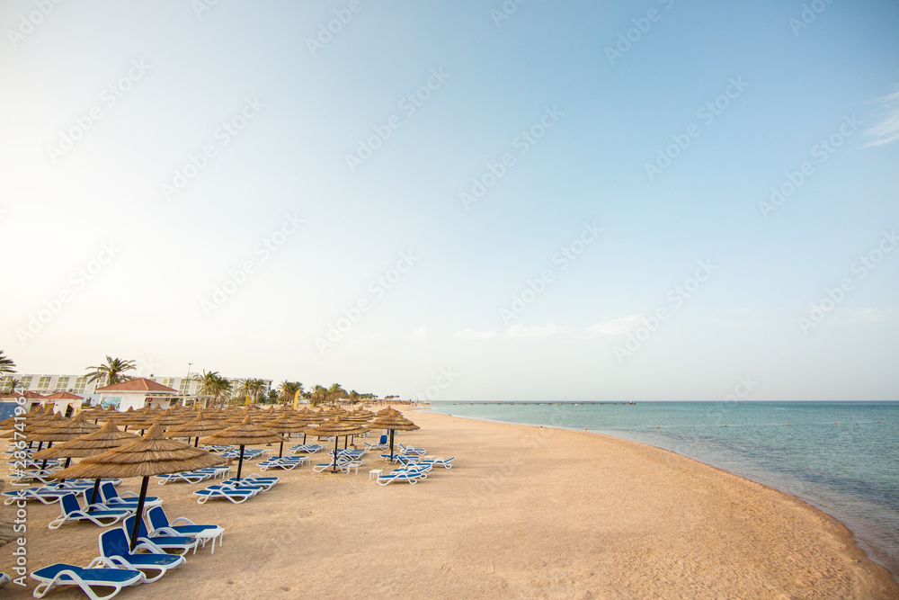Obraz premium Tourist beach with sun loungers and parasols. Red Sea, yellow sand and blue sky. Holidays in Egypt