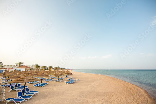 Tourist beach with sun loungers and parasols. Red Sea, yellow sand and blue sky. Holidays in Egypt