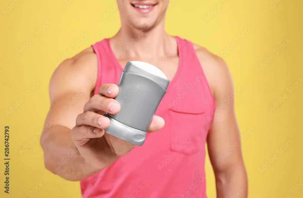 Young man with deodorant on yellow background, closeup Young man with deodorant on yellow background, closeup