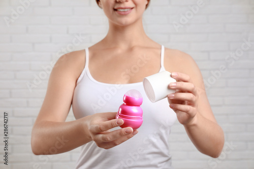 Young woman holding roll-on deodorant against brick wall, closeup