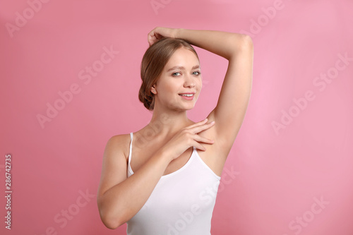 Young woman with smooth clean armpit on pink background. Using deodorant