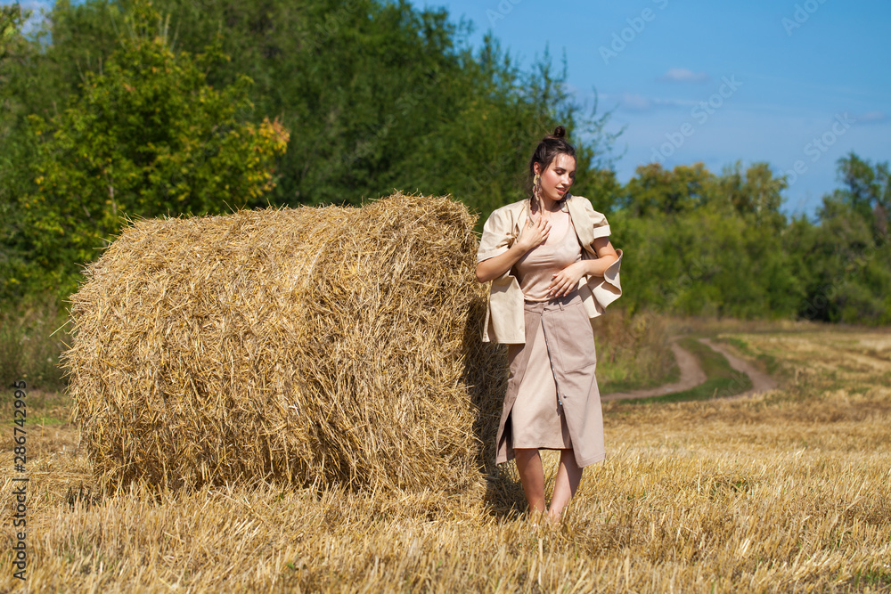 Beautiful girl in a beige suit posing on a background of haystacks in a cut field Beautiful girl in a beige suit posing on a background of haystacks in a cut field